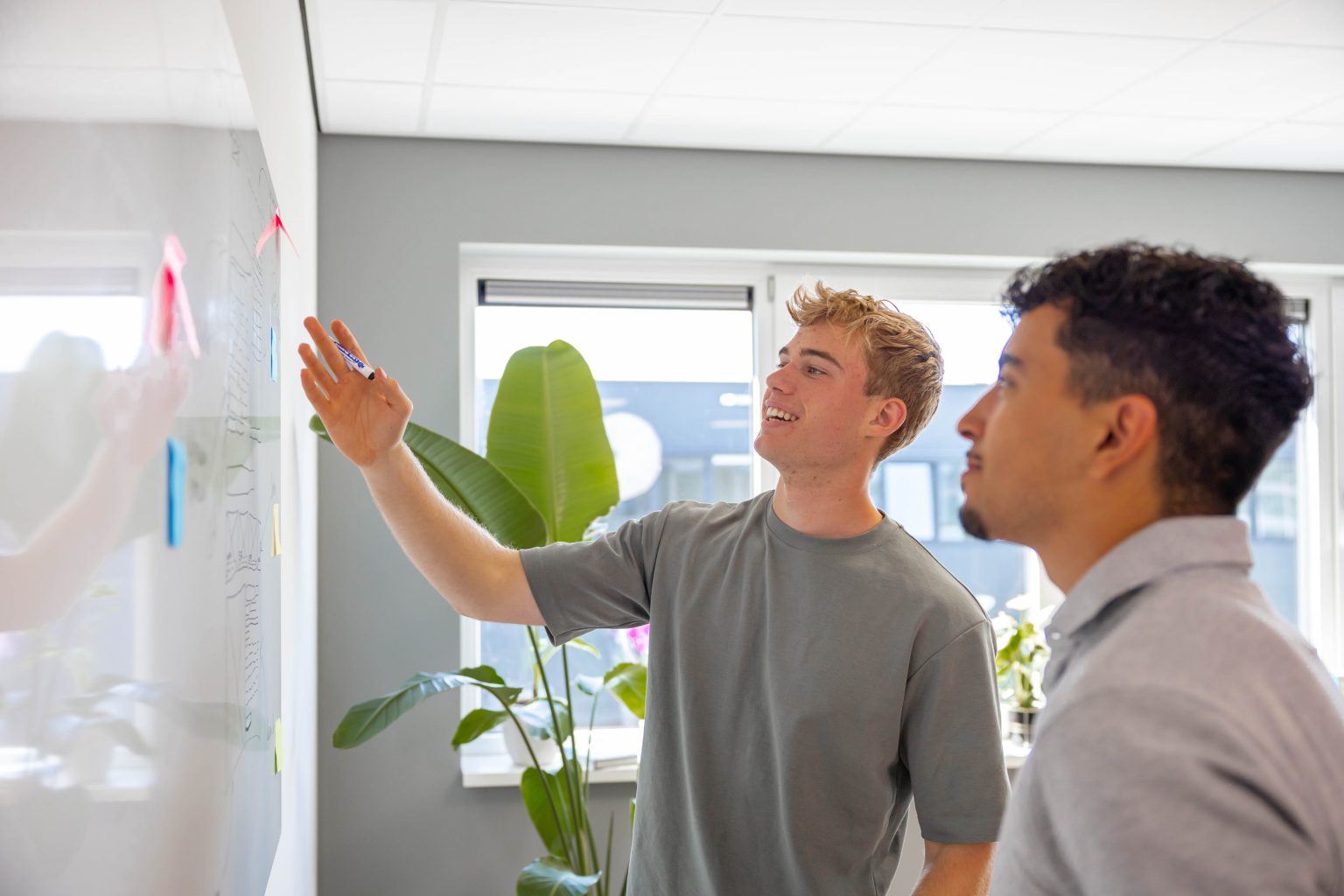 Lars legt aan het whiteboard uit hoe de opzet van een nieuwe website in elkaar zit, een collega kijkt mee