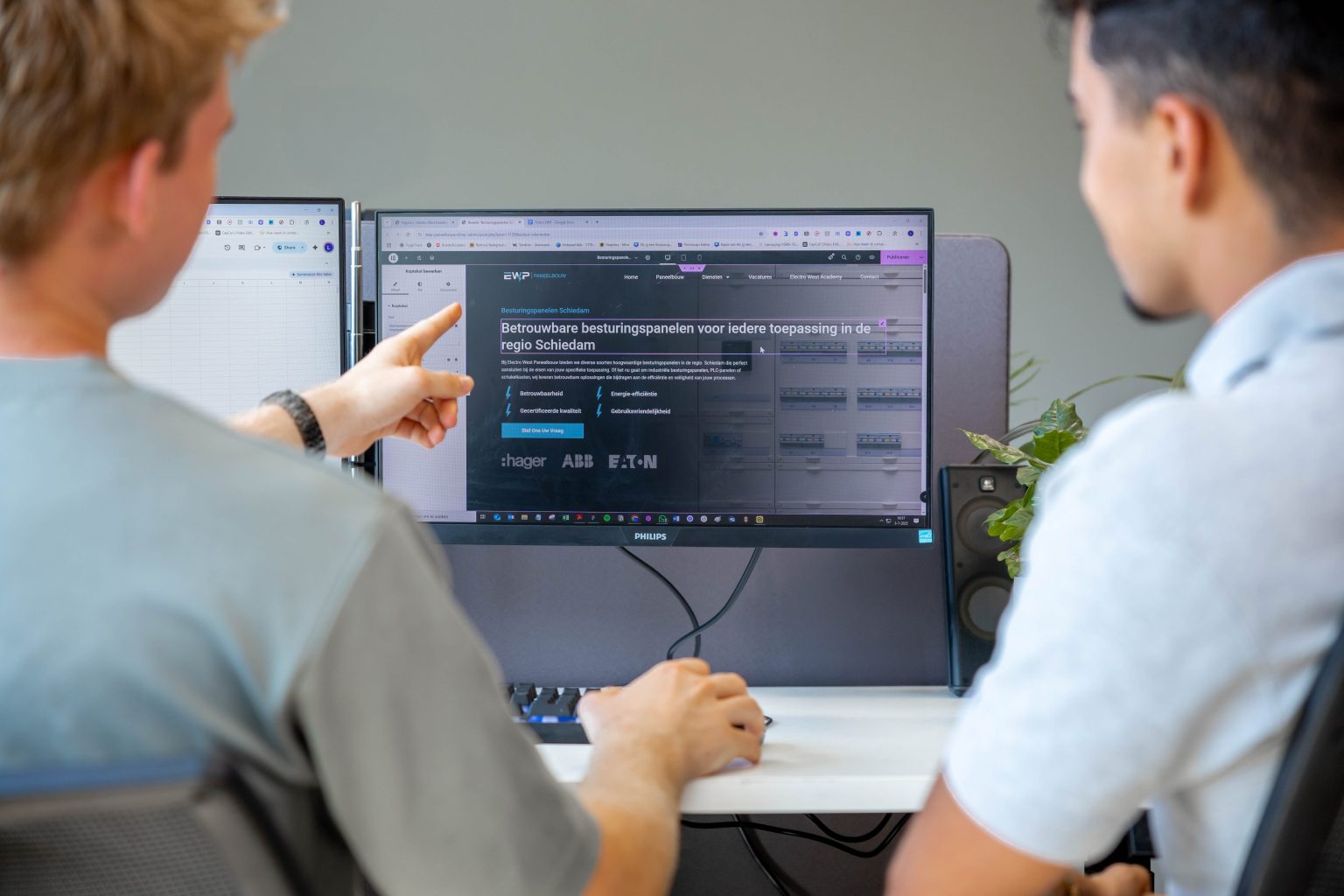 Twee teamleden bespreken een pagina op de monitor en wijzen naar de knop